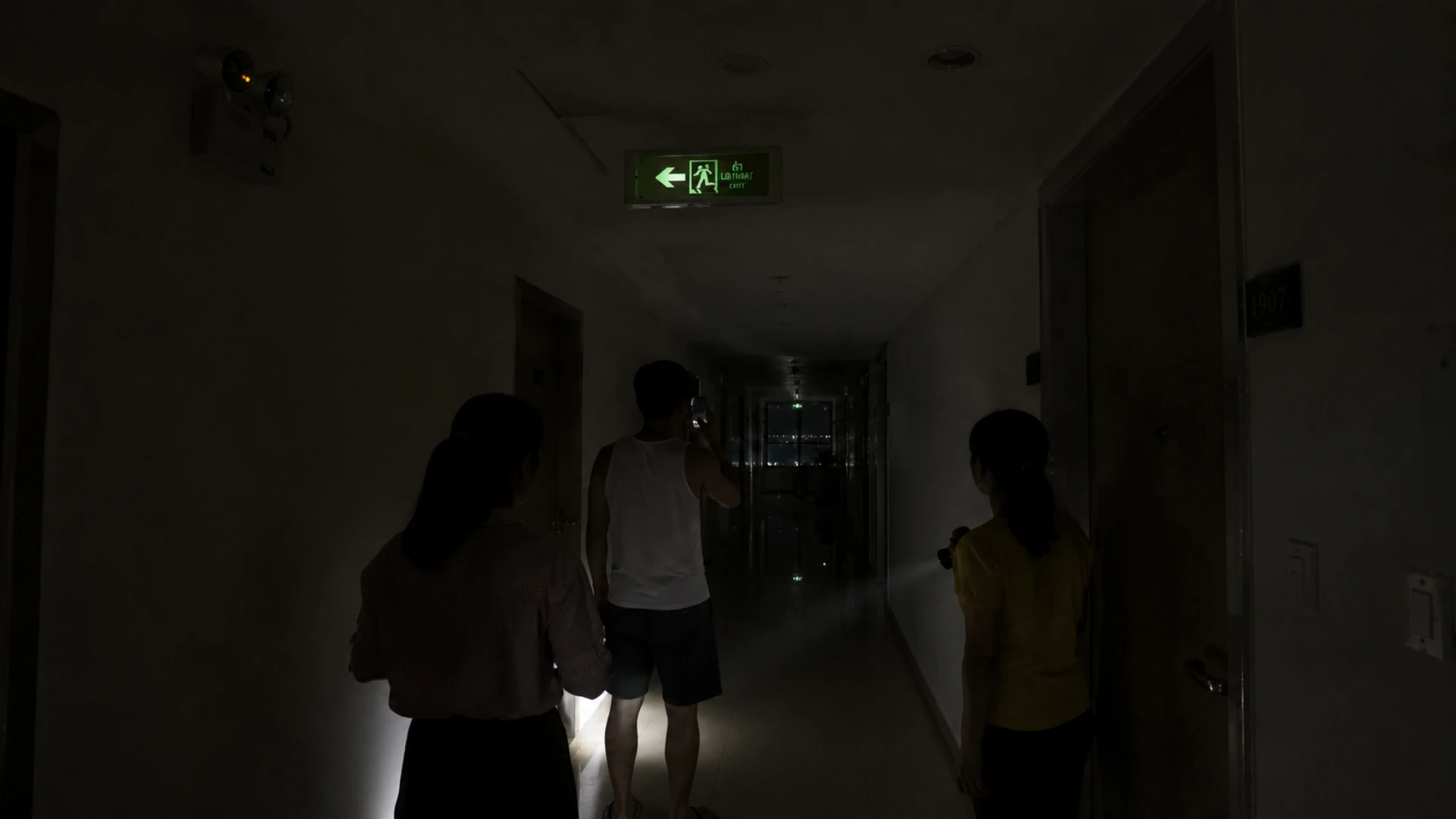 Hành lang tối khi mất điện với đèn EXIT sáng yếu và người đang tìm lối đi