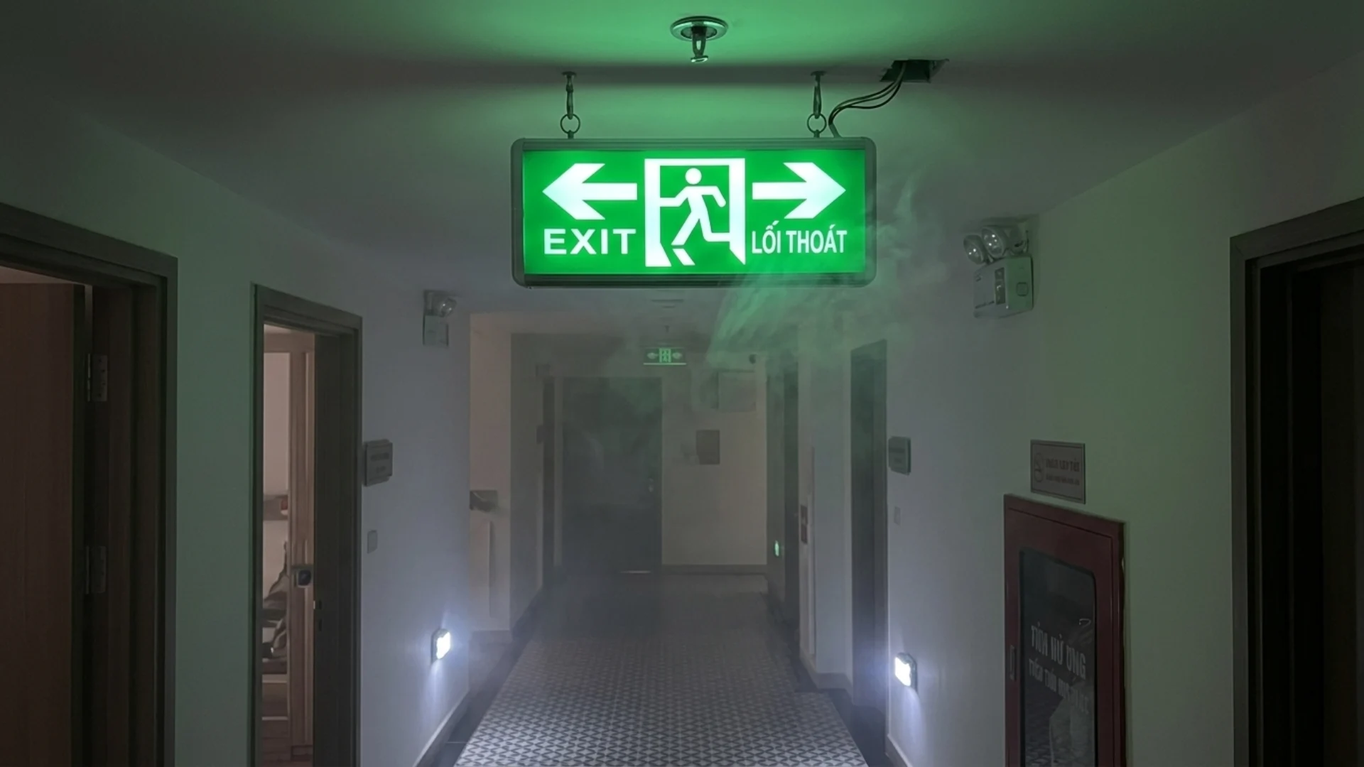 Đèn thoát hiểm màu xanh sáng rõ trong hành lang có khói nhẹ