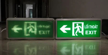 Hai đèn EXIT đặt cạnh nhau với một bên ánh sáng mờ và một bên sáng rõ dễ nhận diện