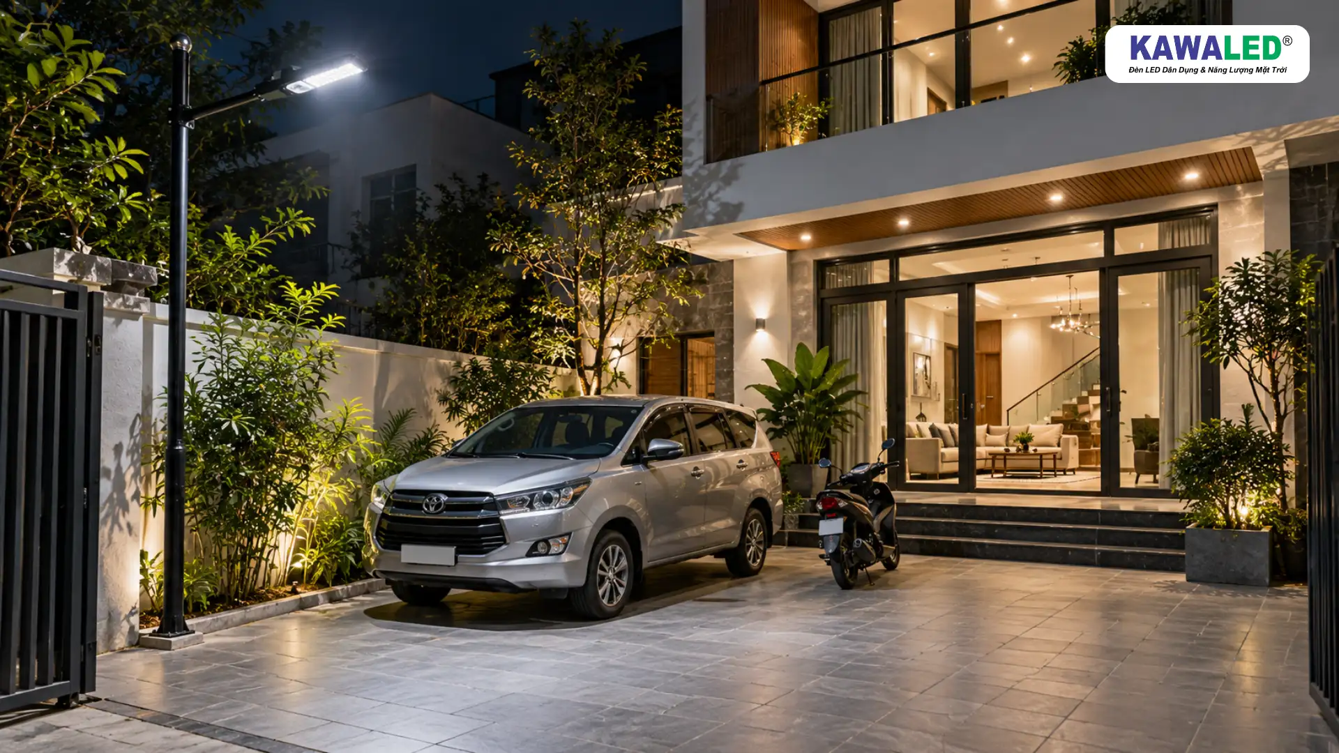 Đèn chiếu sáng sân trước nhà phố có ô tô và xe máy đỗ trên nền gạch xám vào buổi tối.
