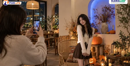 Khách chụp ảnh bằng điện thoại tại góc check-in Halloween có bí ngô và hốc tường hắt xanh dương.